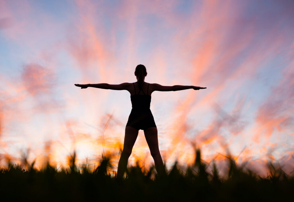 Silhouette of a woman with arms outstretched against a sunset sky