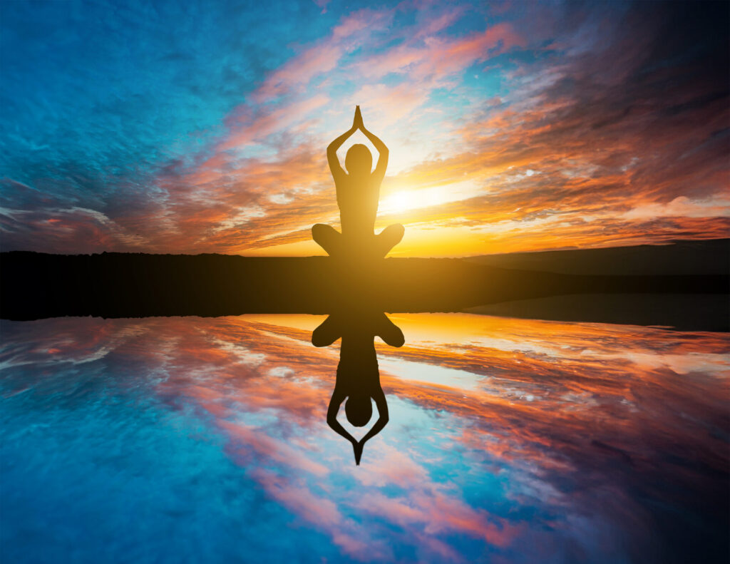 Silhouette of a person meditating in lotus pose, reflected in the water at sunset